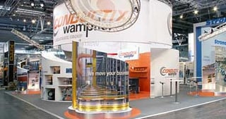 Runder Messestand mit der Aufschrift „Conductix Wampfler“ unter einer abgehängten Ringtraverse. Am Stand steht „We move your business“.